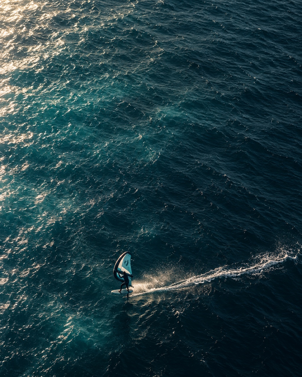 A wing foiler carving a wake across open sea, seen from above